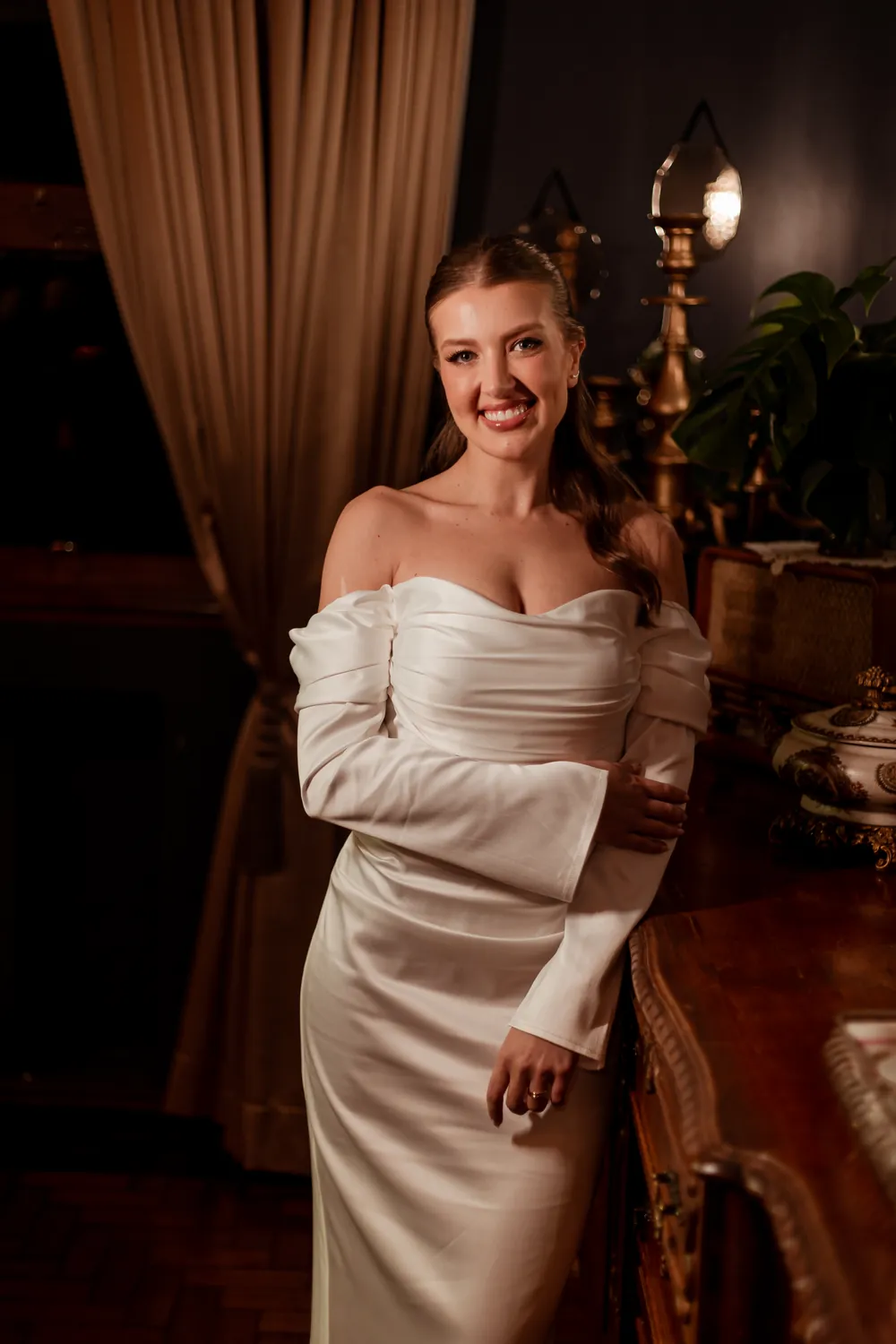 Noiva com vestido de cetim e mangas longas, em ambiente interno